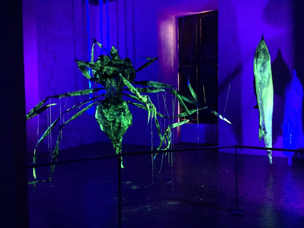 gigantesque araignée fluorescente vert suspendu au plafond dans une salle obscure