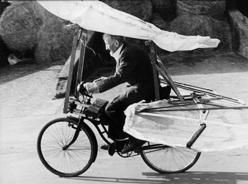 photo en noir et blanc d'un homme agé qui pédale sur son vélo avec des ailes pour prendre son envol