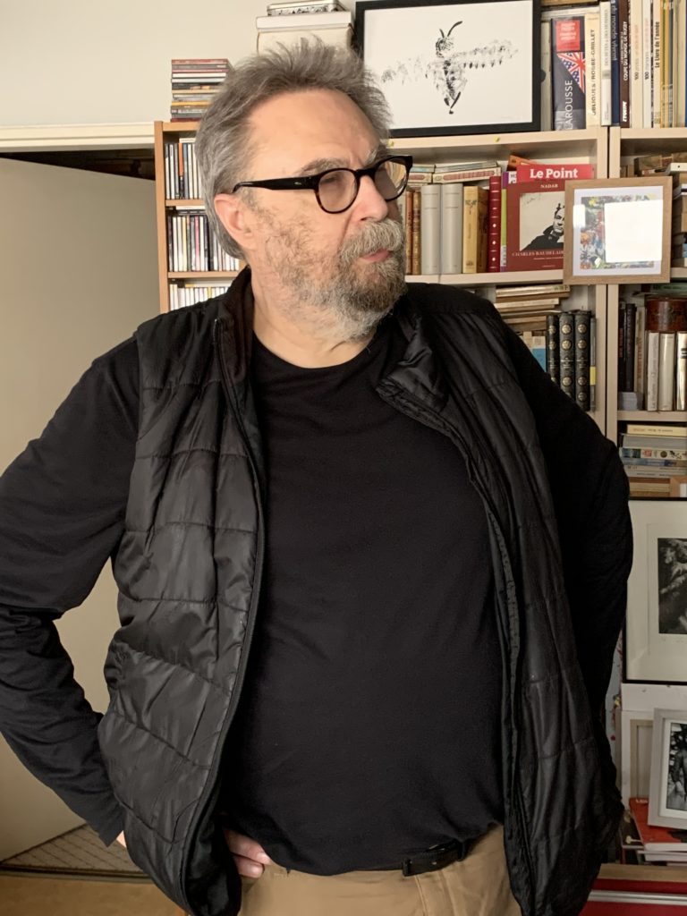 photo de Jacques Cauda debout devant une de ses bibliothèques :