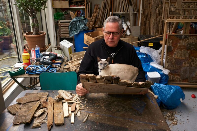 photographie de Marc Bourlier dans son atelier entouré de bois flottés et oeuvres en compagnie de son chat siamois