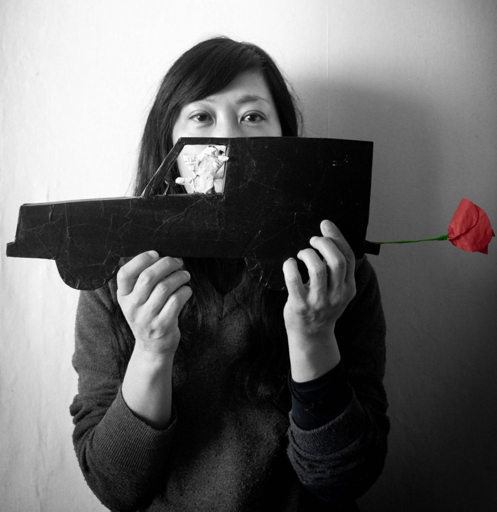 photo noir et blanc du regard de l'artiste Megumi Nemo tenant un camion en carton avec un coquelicot pour pot d'échappement