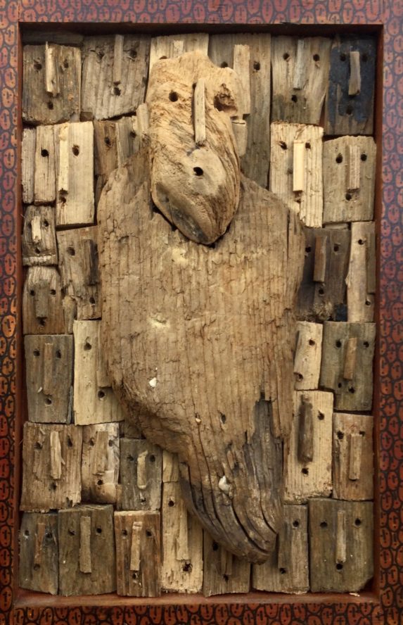 oeuvre en bois flottés de Marc Bourlier représentant un homme solitaire devant un ensemble de visages, cadre dessiné de visages