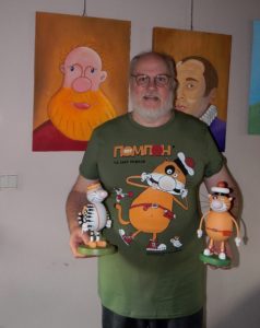 image qui représente l'artiste Guy Pirot, devant deux de ses tableaux et portant deux sculptures