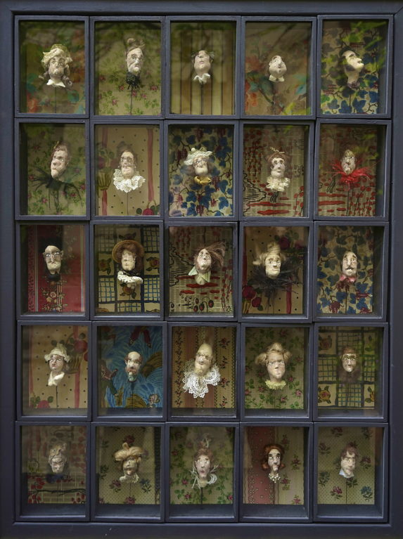 image d'une boîte en bois bleue avec 25 casses vitrées comportant chacune un buste sur fond de papier peint