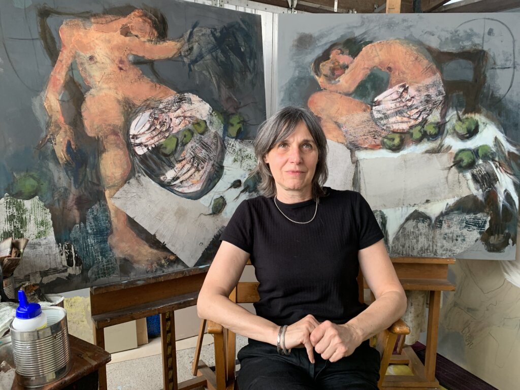 image qui représente la peintre Sylviane Blondeau assise de vant deux toiles pentes